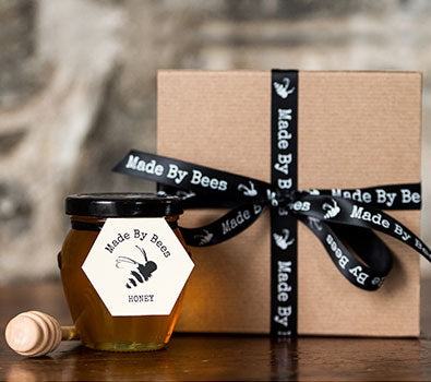 A jar of Made by Bees honey beside a gift box with a black bow